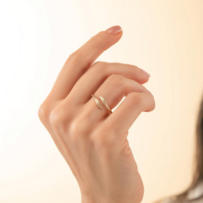 A close-up of a hand wearing a gold ring with a leaf-like design.