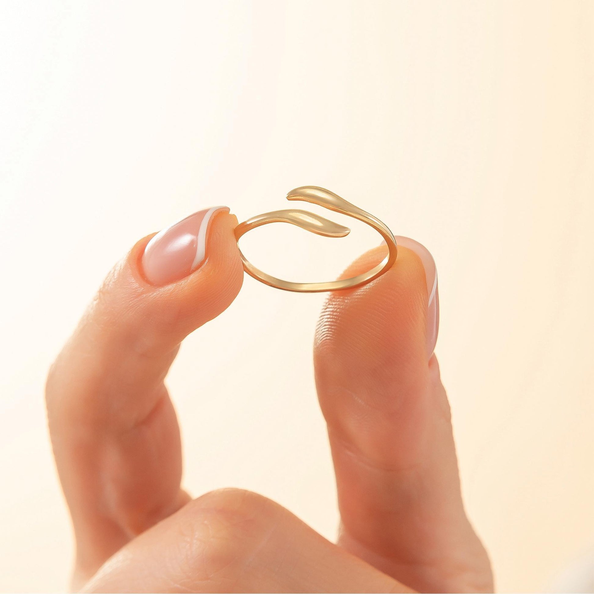 A close-up image of a person's hand holding a gold ring with a unique design.