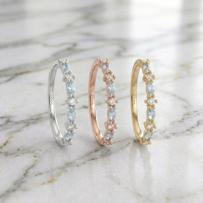 Three solid gold rings with aquamarine marquise and round moissanite stones are displayed on a marble surface.