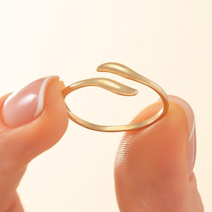 A close-up image of a person's fingers holding a gold ring with a leaf-like design.