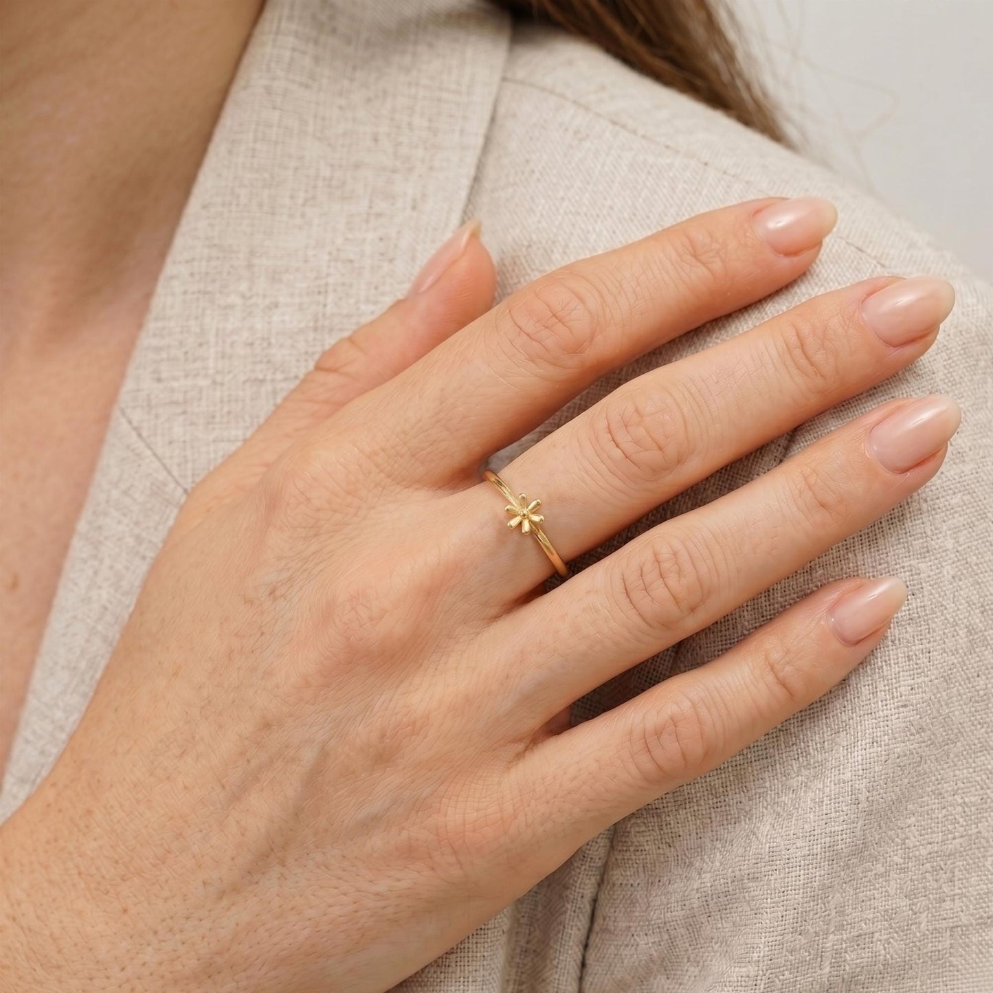 A close-up of a person's hand wearing a gold ring with a flower design.
