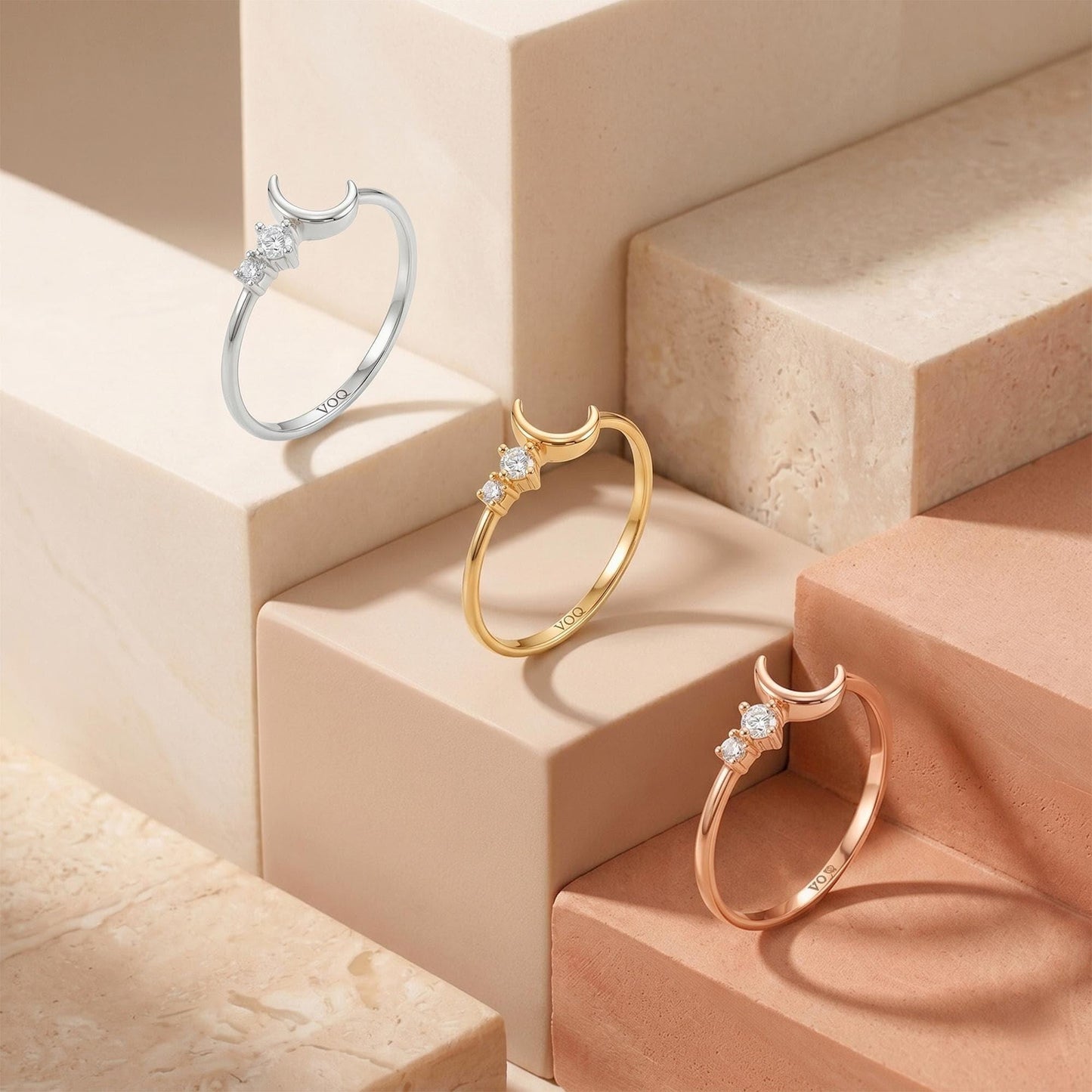 Three rings with crescent moon designs are displayed on marble steps, showcasing their unique designs and colors.