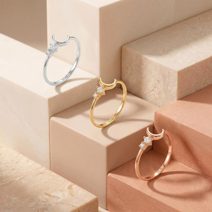 Three rings with crescent moon designs are displayed on marble steps, showcasing their unique designs and colors.