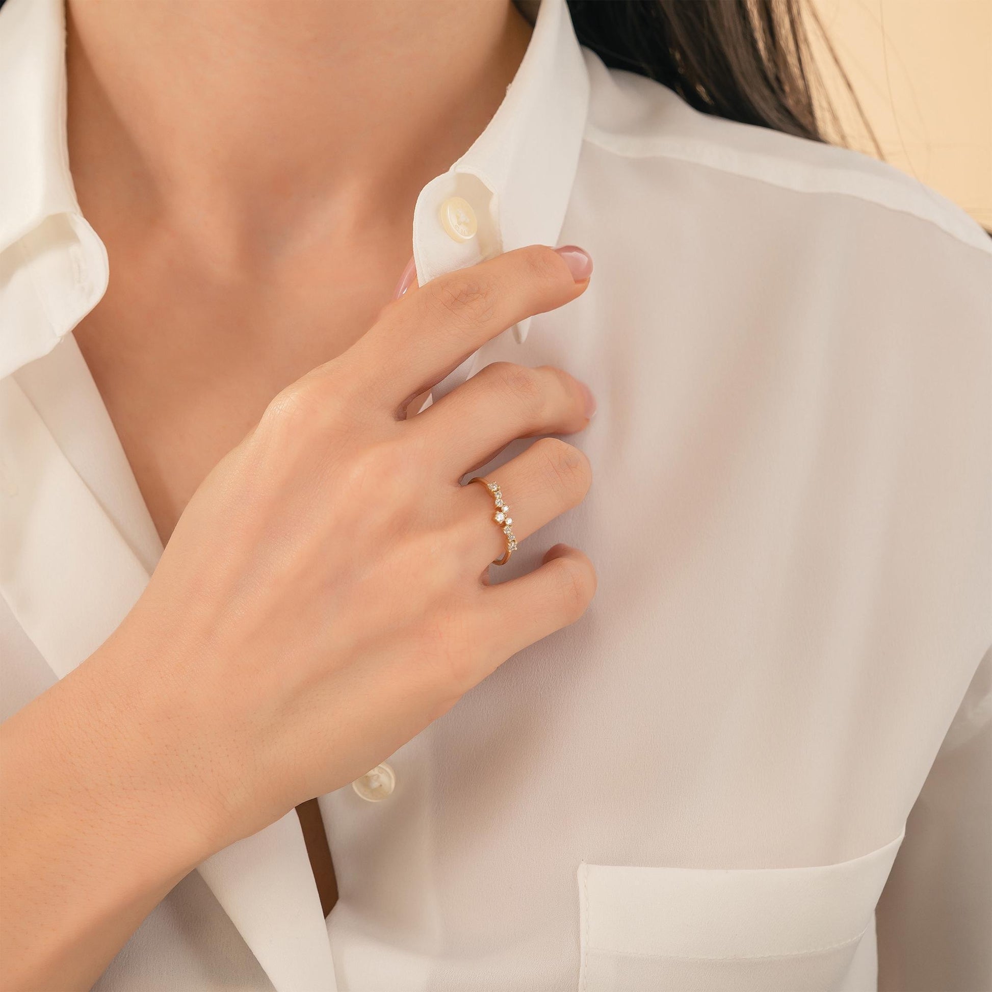 A close-up of a person's hand wearing a gold ring on their finger, with their hand adjusting the collar of a white shirt.