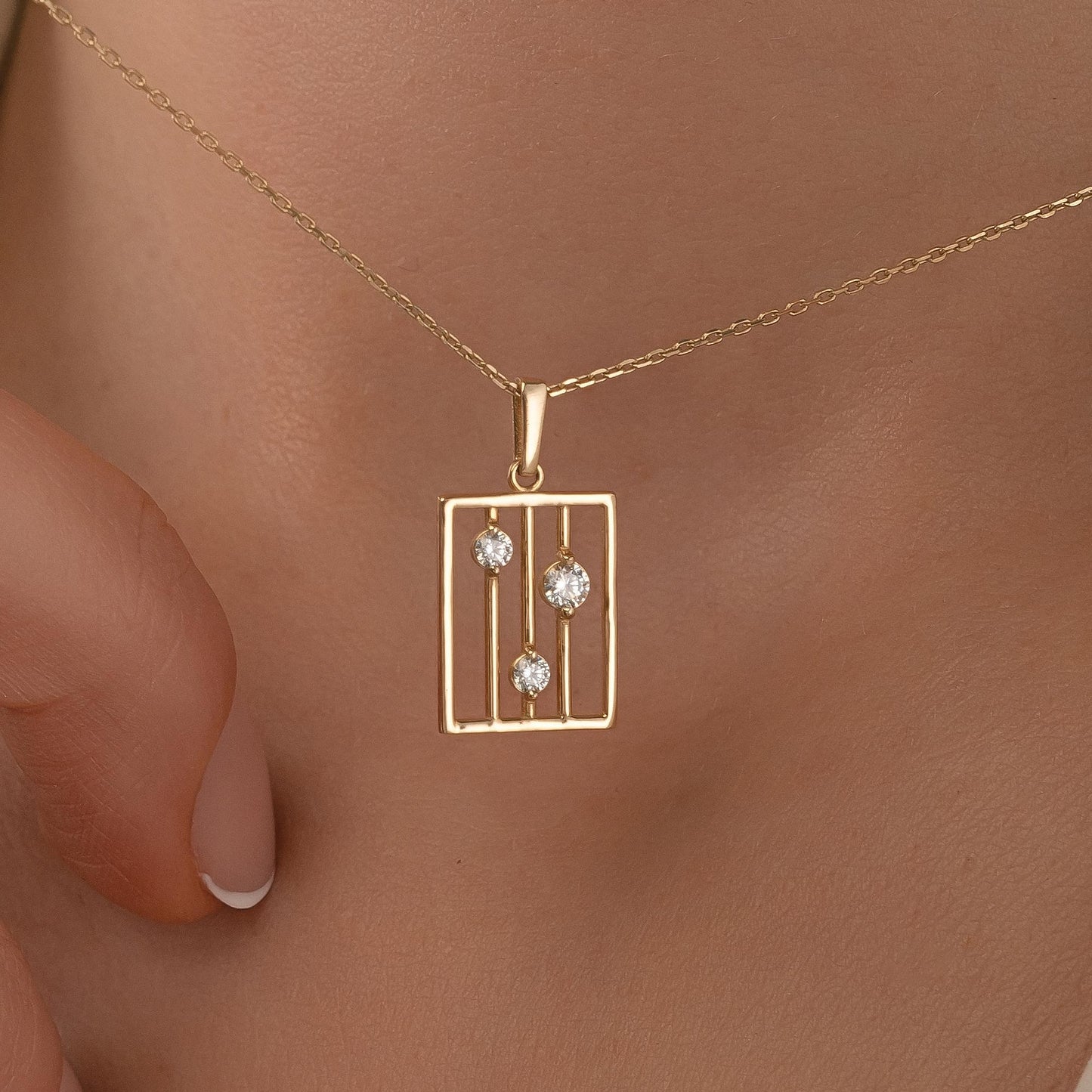 A gold necklace with a pendant featuring three diamonds arranged in a square pattern.