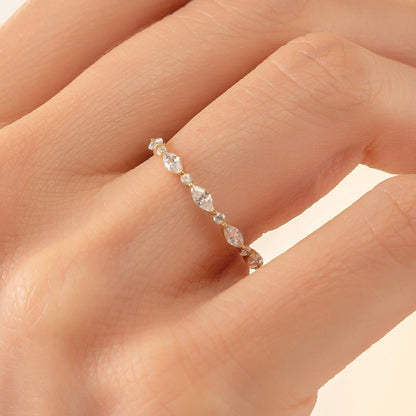 A close-up of a person's hand wearing a delicate gold ring with a row of small, clear gemstones.