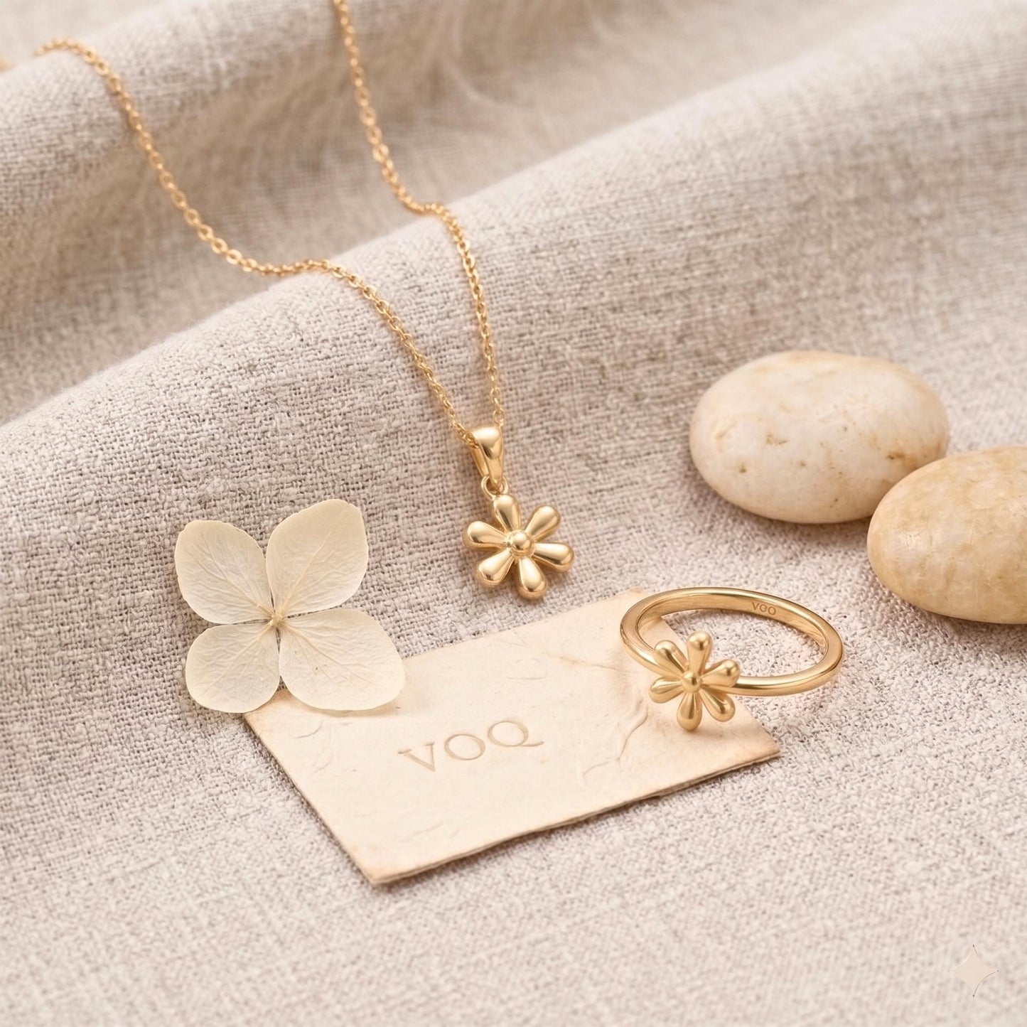 a collection of gold jewelry, including a necklace, pendant, ring, and flower, arranged on a beige fabric surface.