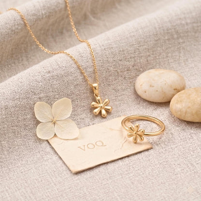 a collection of gold jewelry, including a necklace, pendant, ring, and flower, arranged on a beige fabric surface.