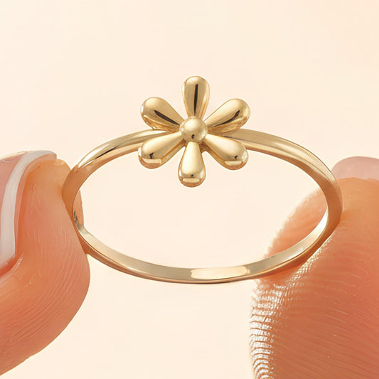 A close-up of a gold ring with a flower design, held between two fingers.