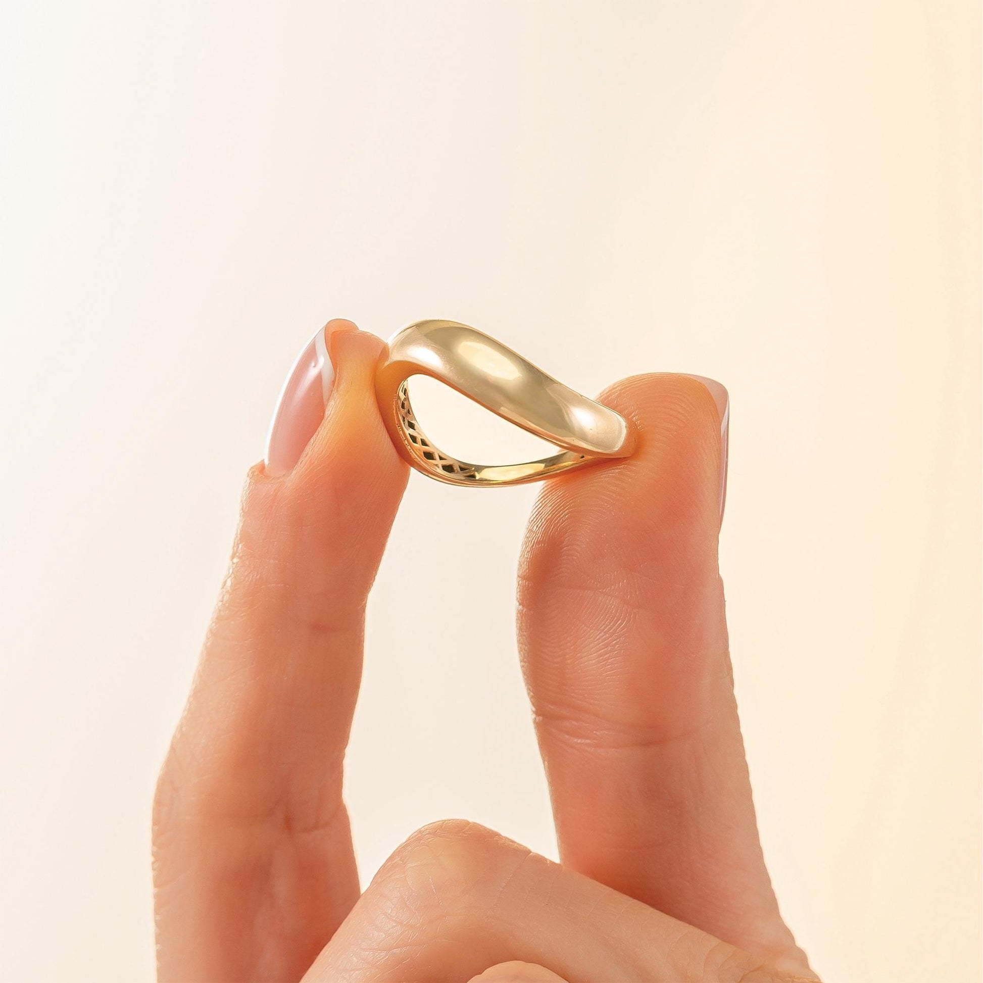 A hand holding a gold ring against a light background.
