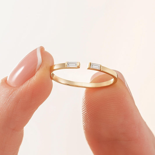 A gold ring with two diamond-encrusted stones is being held between two fingers.