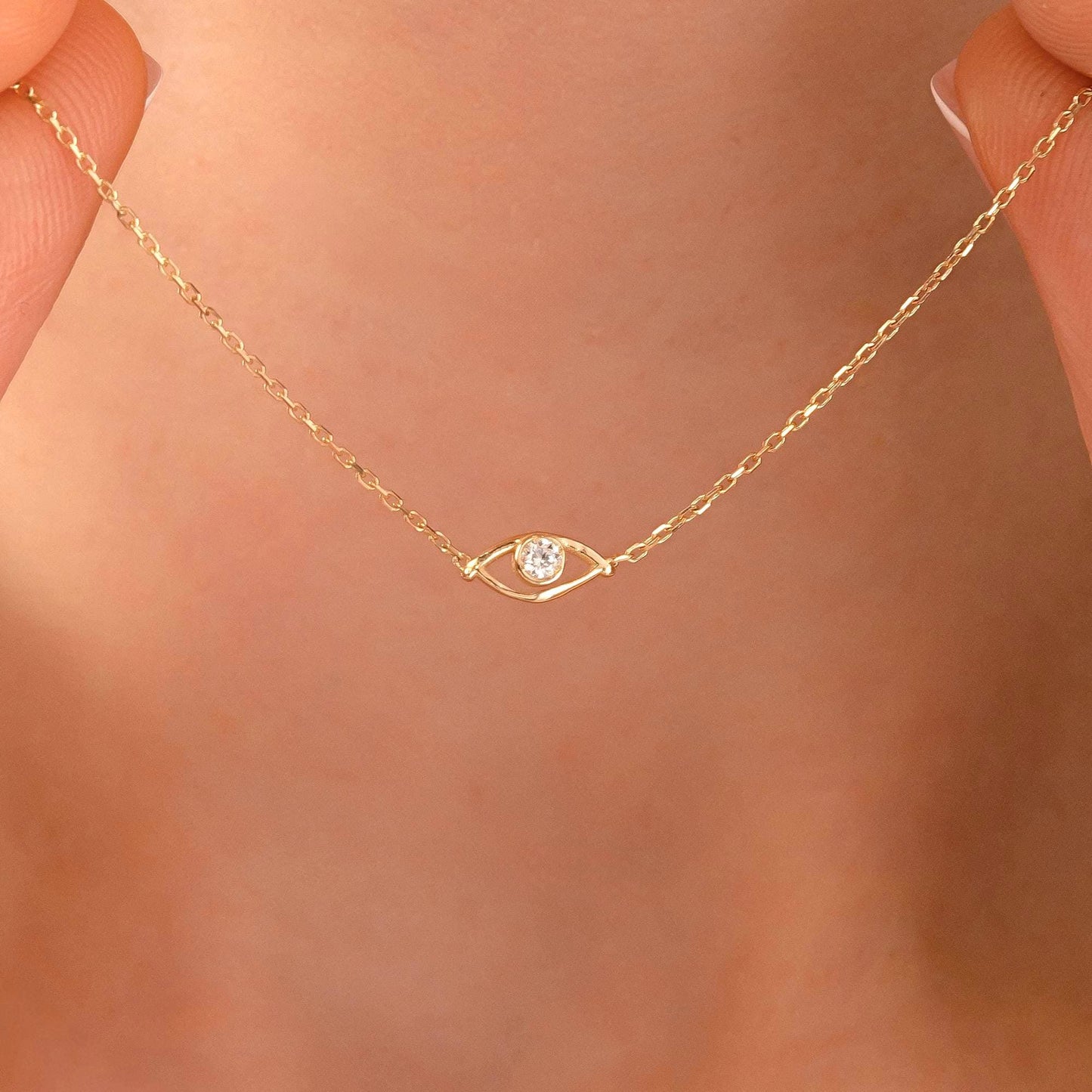 A close-up view of a delicate gold necklace with a small diamond pendant, held between two fingers.