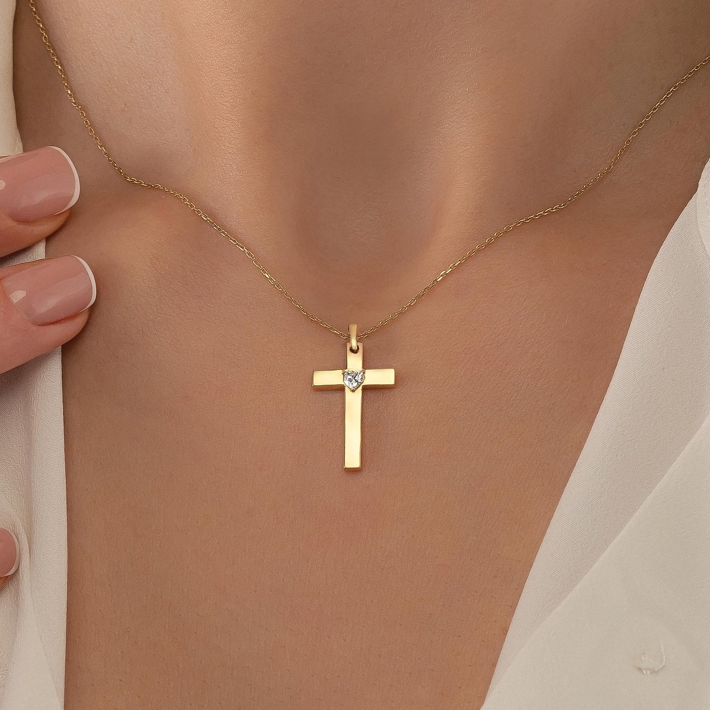 A gold cross pendant with a diamond set in the center is displayed on a person's neck.