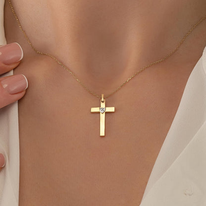 A gold cross pendant with a diamond set in the center is displayed on a person's neck.