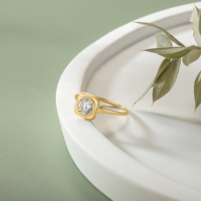 A gold ring with a large diamond sits on a white plate, accompanied by a green leaf.