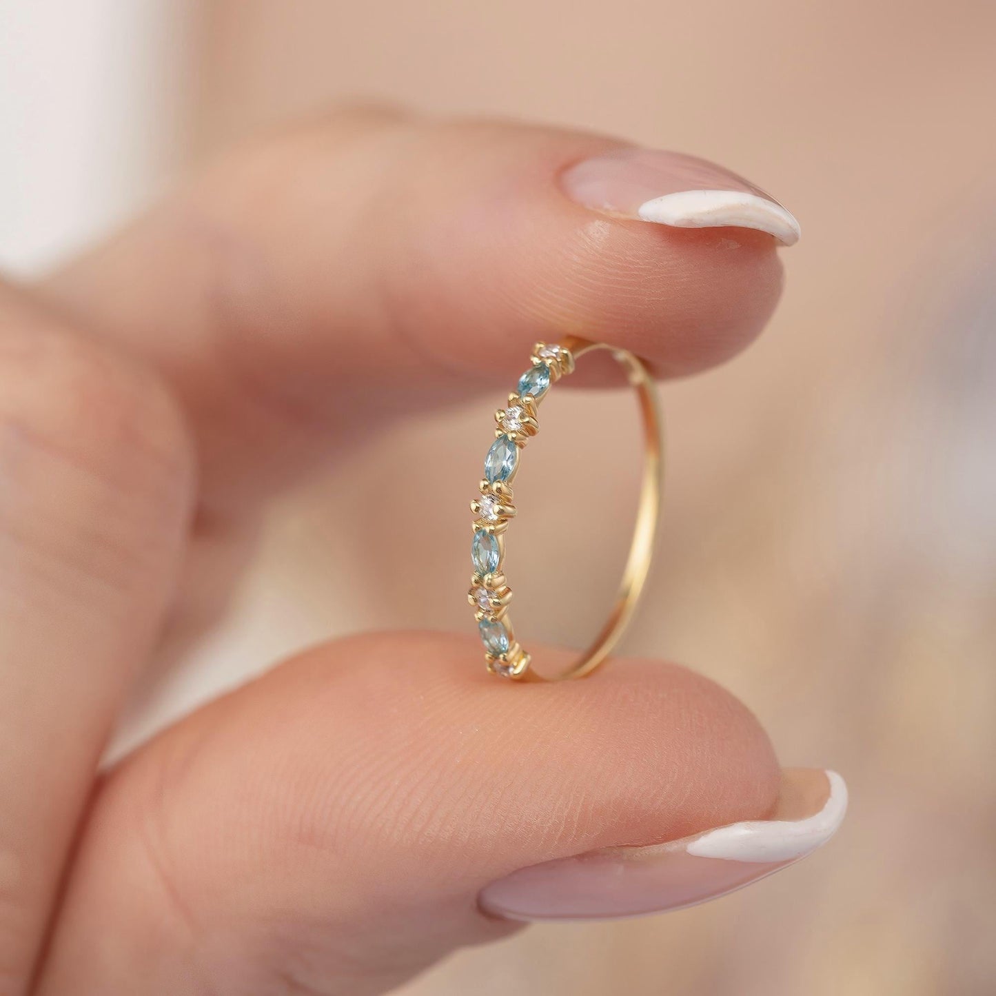 A close-up image of a person's hand holding a gold ring with aquamarine marquise and round moissanite stones.