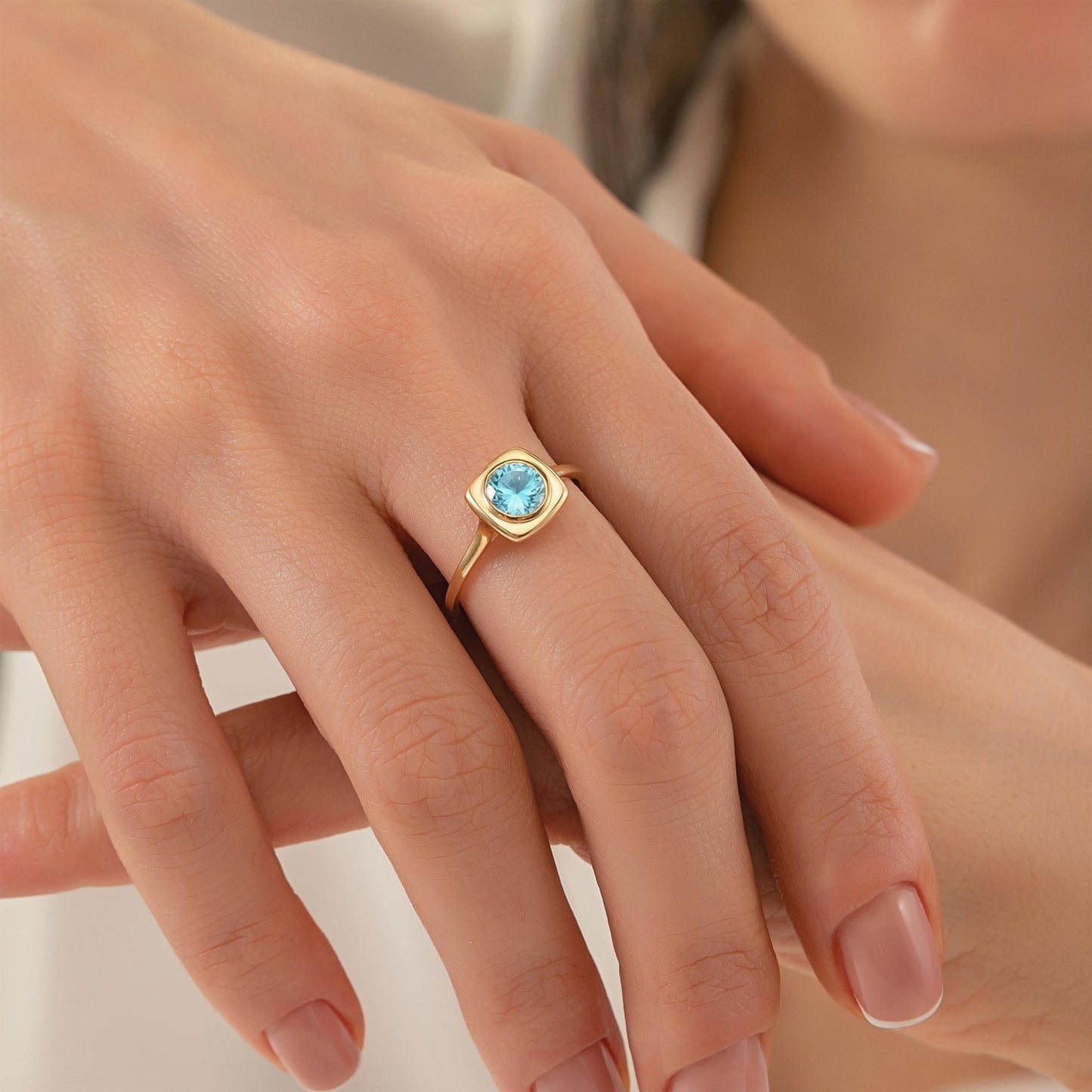 A close-up image of a person's hand wearing a gold ring with a blue gemstone.