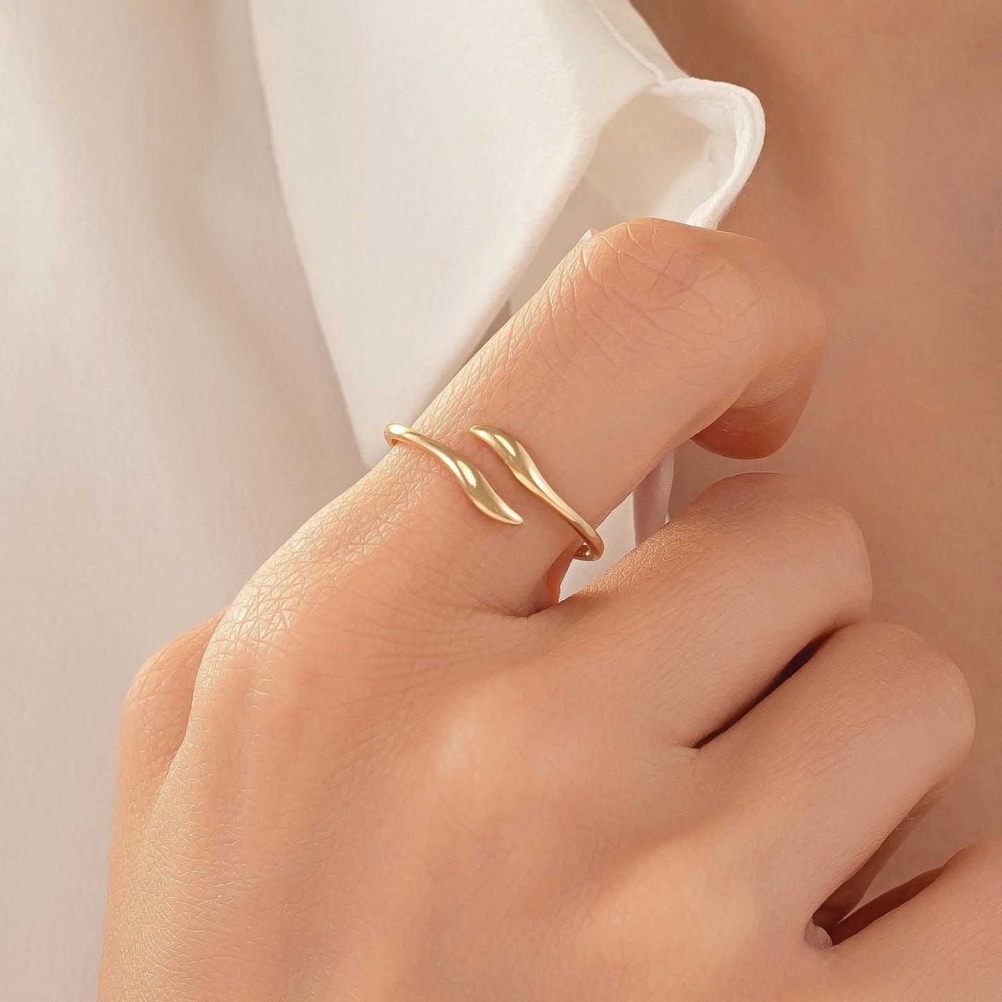 A close-up of a person's hand wearing a gold ring with a leaf-like design.