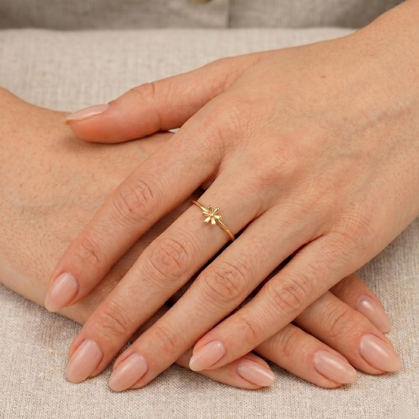 A close-up image of a person's hands with a gold ring featuring a small flower design.
