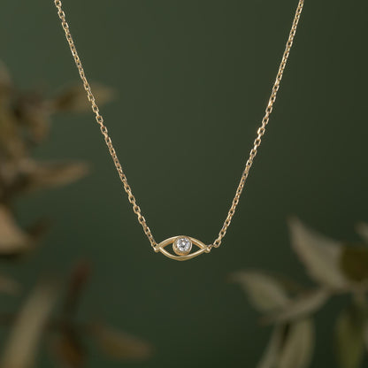 A delicate gold necklace with a small diamond pendant in the center, set against a blurred green background.