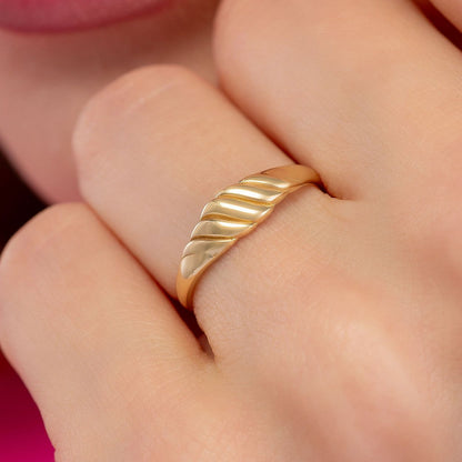A close-up of a person's hand wearing a gold ring with a curved band.